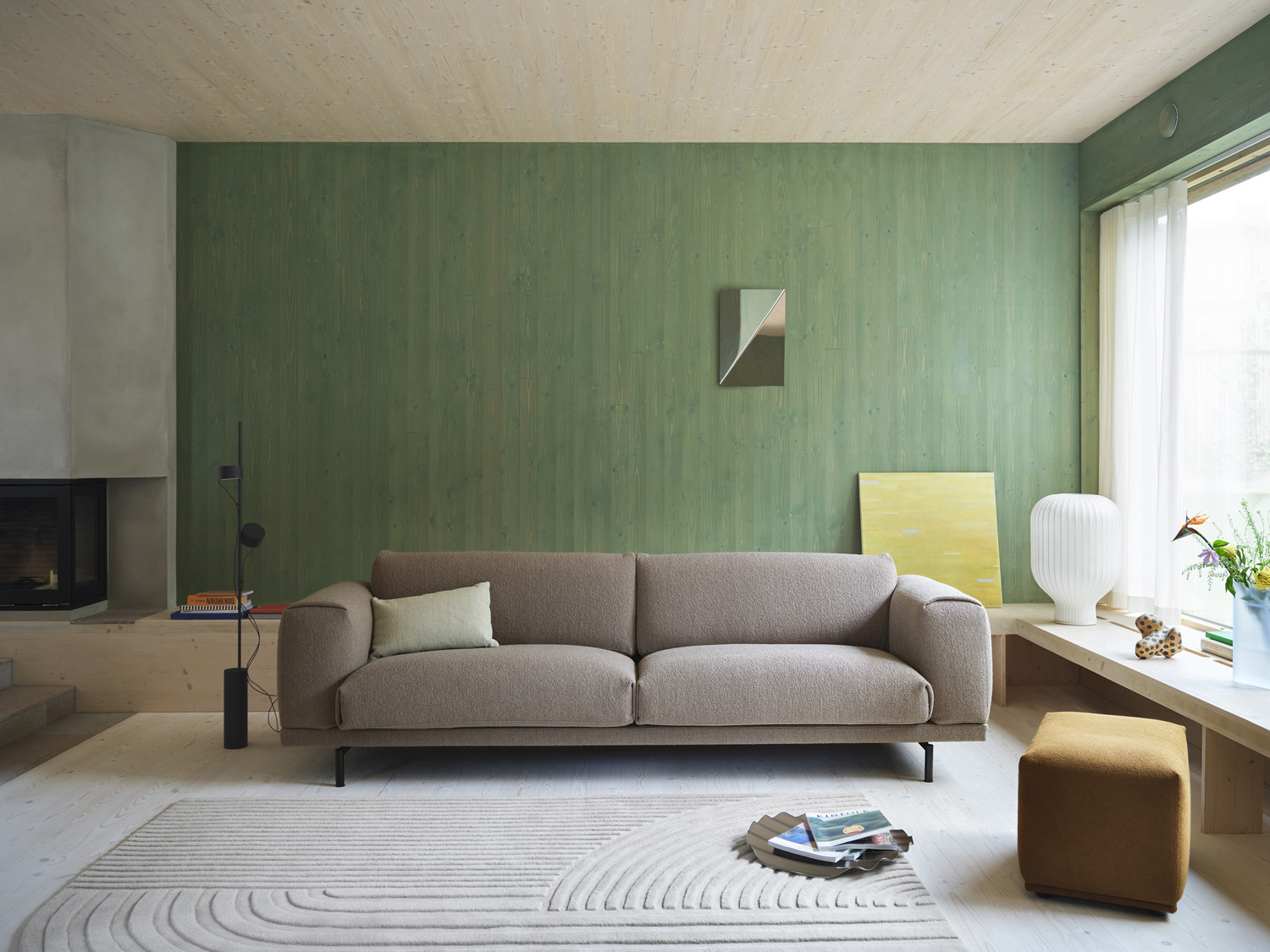 The Muuto Rest Sofa is elegantly styled with a burnt orange Relevo Rug and complemented by a Strand Table Lamp. A Gaze Mirror hanging on the wall adds a sophisticated, sculptural ambiance to the room.