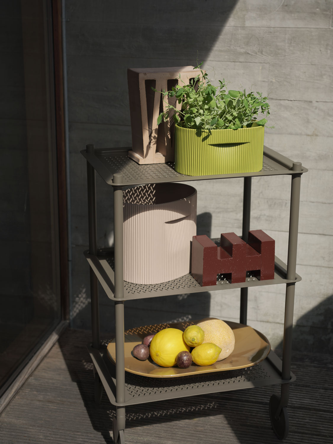 A Muuto setting featuring a Flow trolley 3 layer in taupe. The trolley is styled with a Ridge planter 13 cm in moss green and 24 cm in beige and a Mere bowl in brown green. The combination of modern and natural elements creates a sophisticated and functional arrangement.