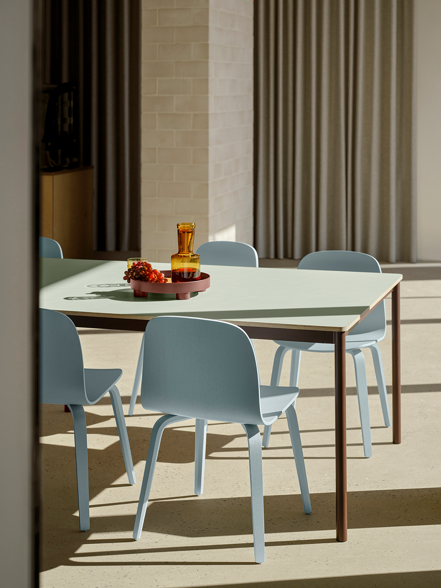 A base table in light green, brown, and red tones, paired wit  light blue Visu chairs placed in the sunlight. 