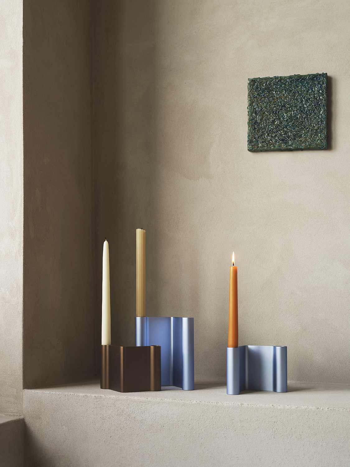Modern candle holders in various colors are arranged on a shelf, adding vibrant accents to the grey stonewashed walls.