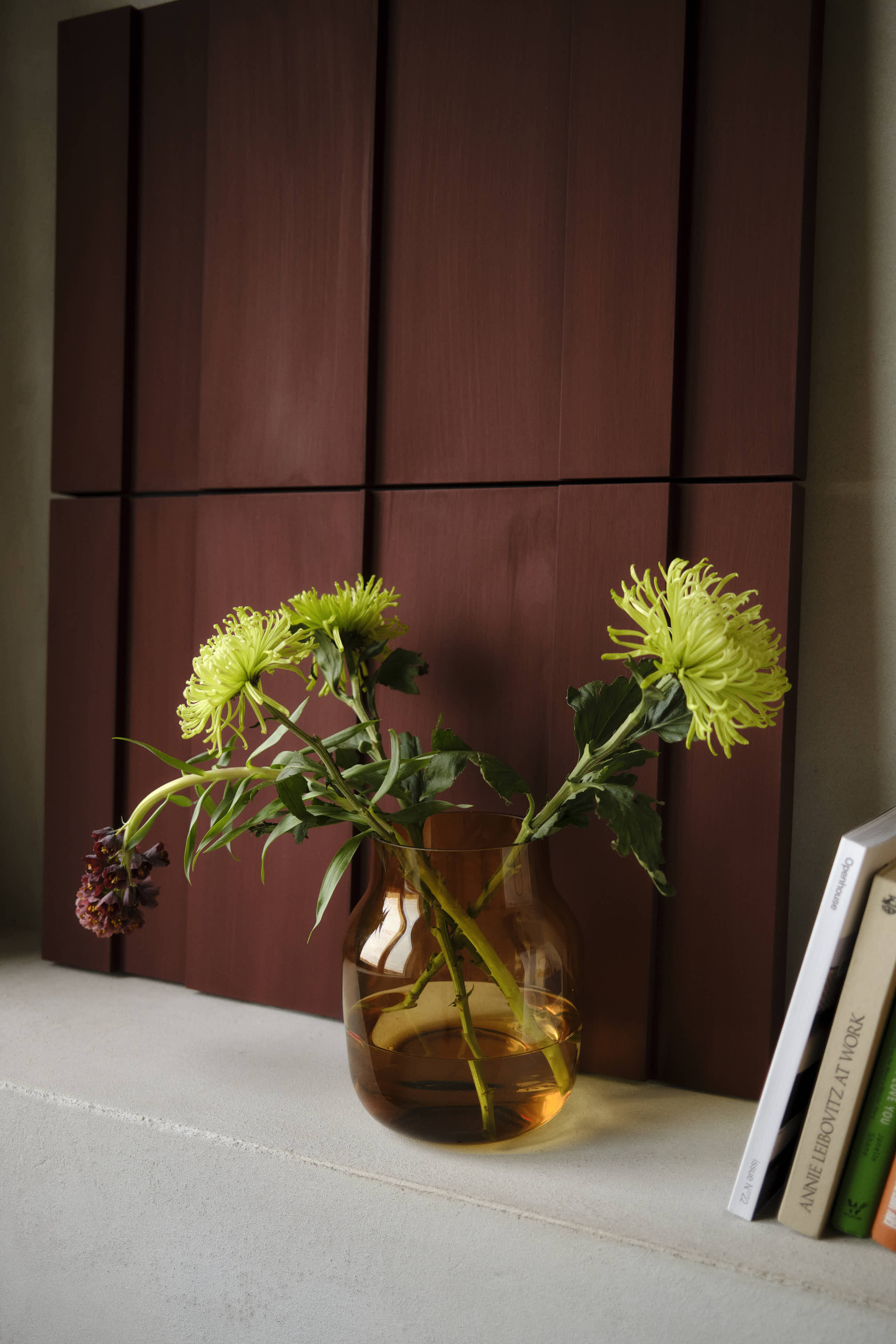 A classic, simple glass vase in a warm burnt orange color, elegantly styled with fresh flowers, adding a vibrant touch to the arrangement.