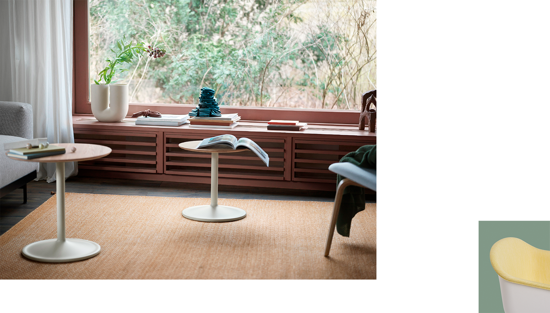 Living room setting with two Soft Side Tables in neutral tones. A large window seat with books, decorative objects, and a Kink vase frames a view of the garden outside. Calm and minimalist atmosphere with warm, muted colors.